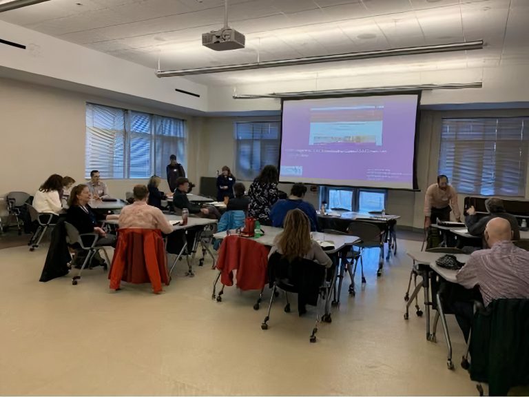 Group of participants sit at tables looking at a presentation screen during a New Hampshire State Coordinating Council for Community Transportation ( SCC ) meeting with NH Health and Human Service Temporary Assistance for Needy Families staff.