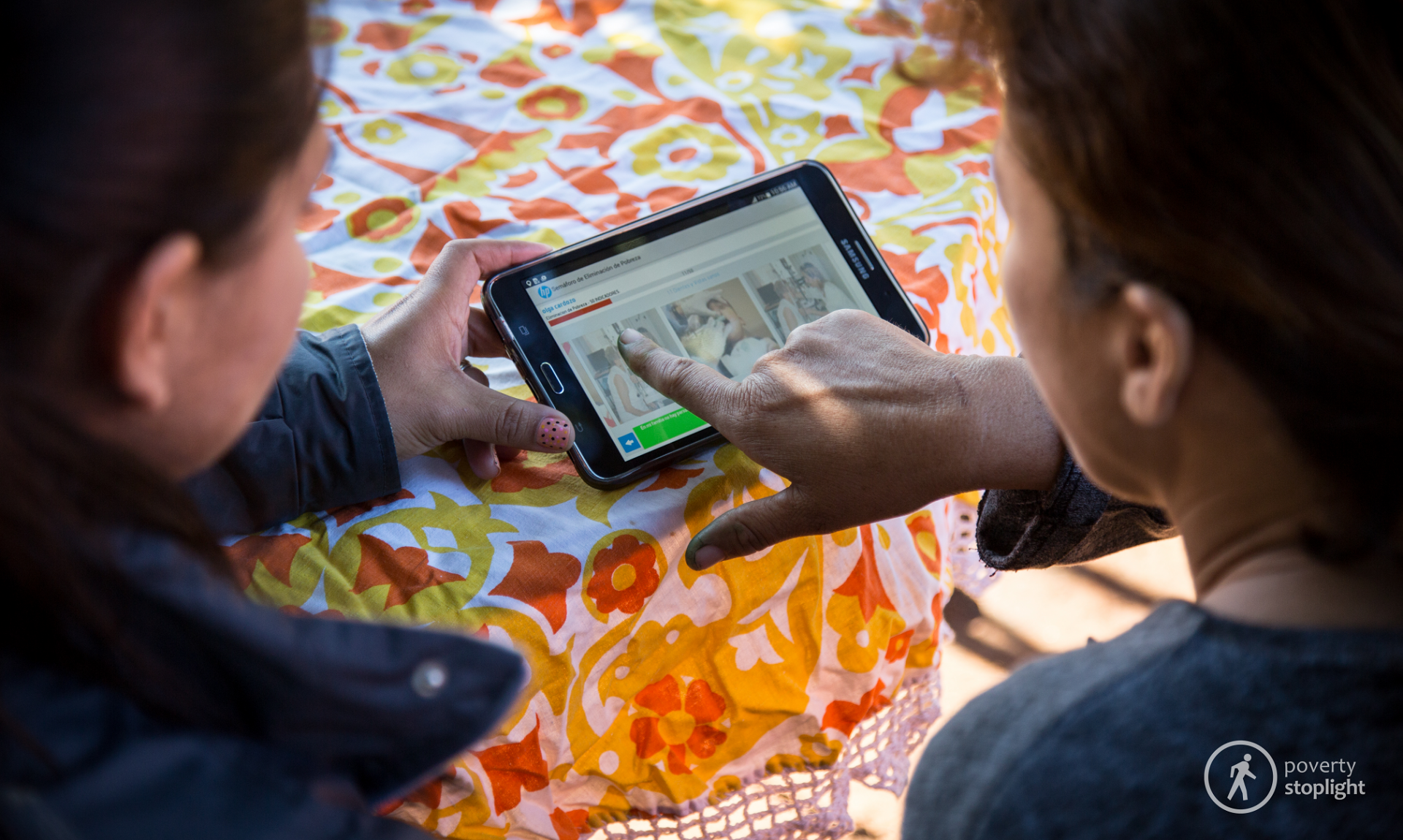 Two people hold and look at a tablet with the poverty spotlight tool.