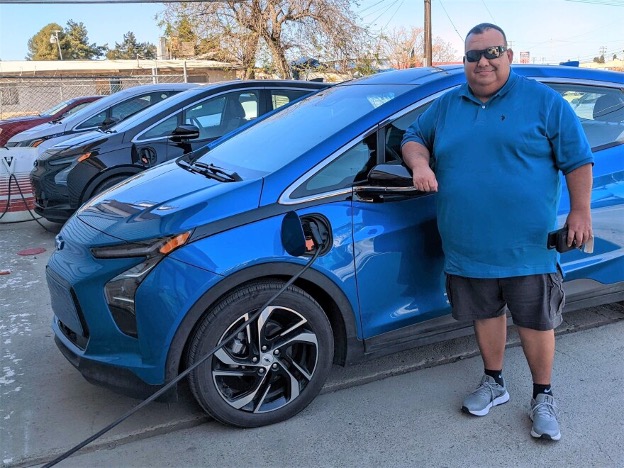 Man standing next to blue electric car plugged in and charging.
